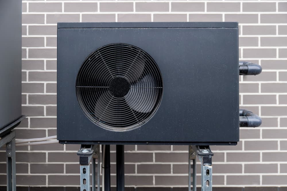 Exterior view of a modern black heat pump unit installed against a brick wall, highlighting professional heat pump service in Thornton, CO.